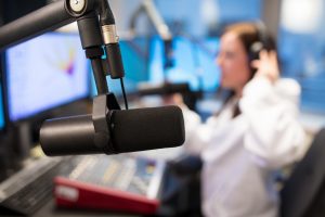 mikrofon v rádiu v pozadí s moderátorkou nasazující si sluchátka a vysílající v rádiu