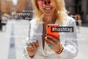 usměvavá blondýnka ve slunečních brýlích držící chytrý telefon a označující hashtagy
